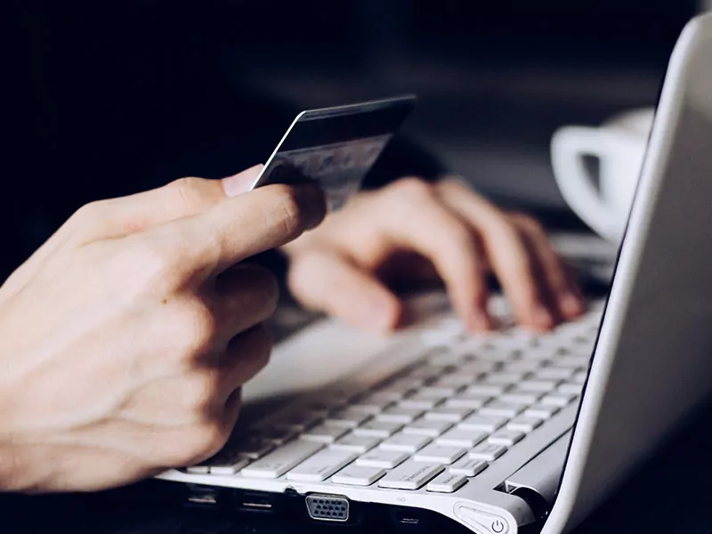 person using laptop and holding a credit/debit card in other hand